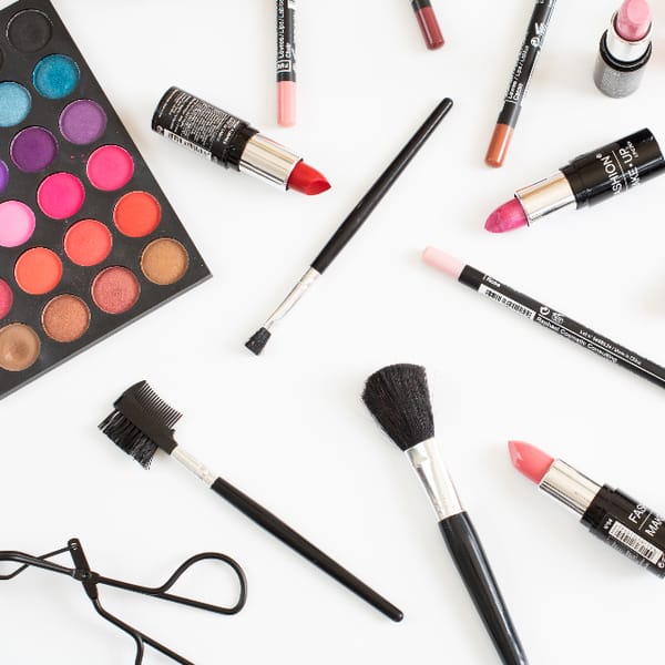 Paleta de sombras, labiales y brochas de maquillaje sobre fondo blanco